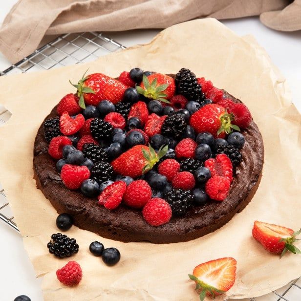 Kladdkake med dadler toppet med friske bær, liggende på et bakepapir på rist.
