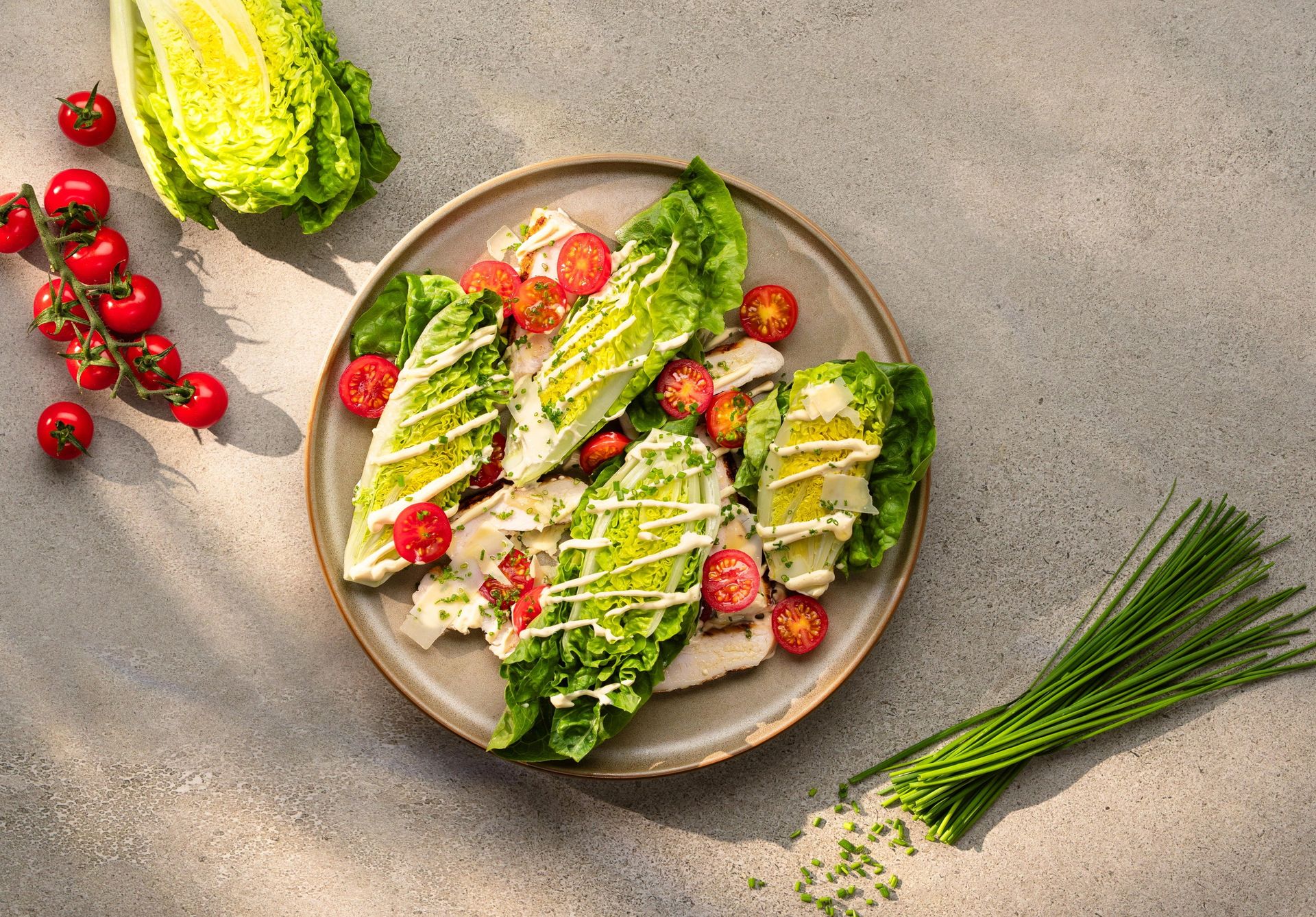 Hjertesalat med cæsardressing, parmesan og cherrytomater servert på et fat.