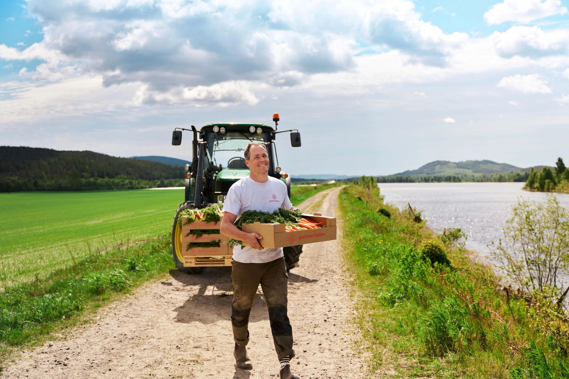 Bonde med en kasse gulrøtter foran en traktor.