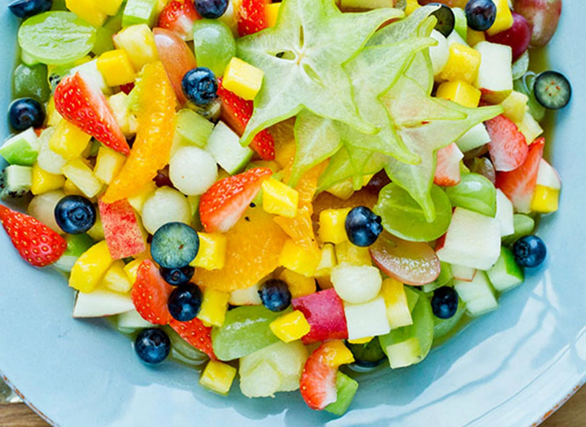 Fruktsalat med stjernefrukt, jordbær, druer, blåbær, melon og kiwi på et blått fat
