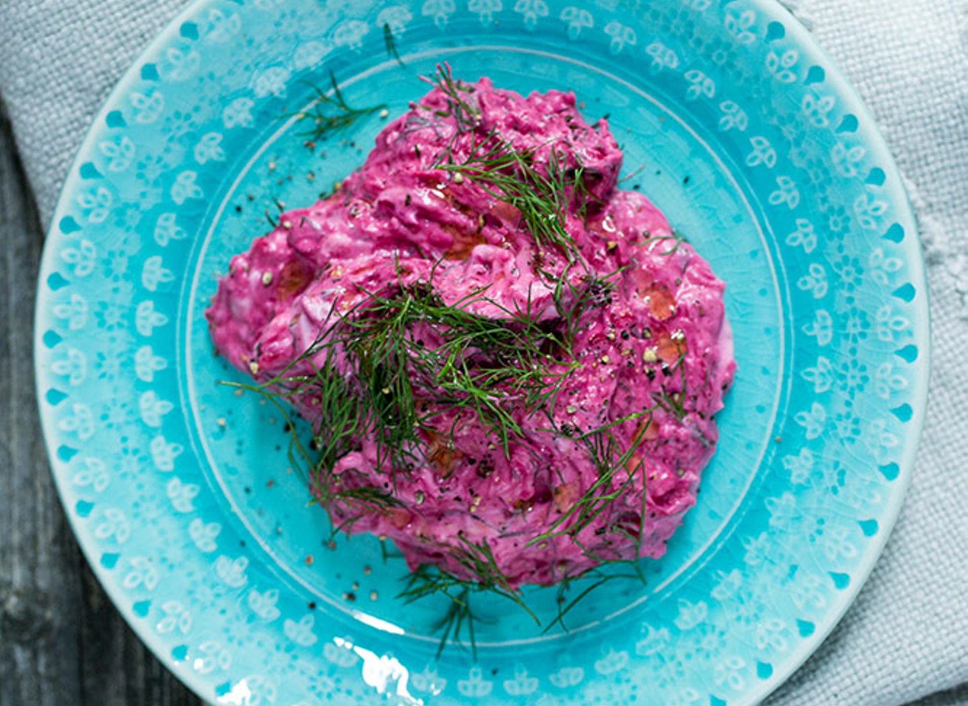 Kremet rødbet tzatziki med små biter av grønnsaker servert på en turkis tallerken, toppet med frisk dill og et dryss pepper.