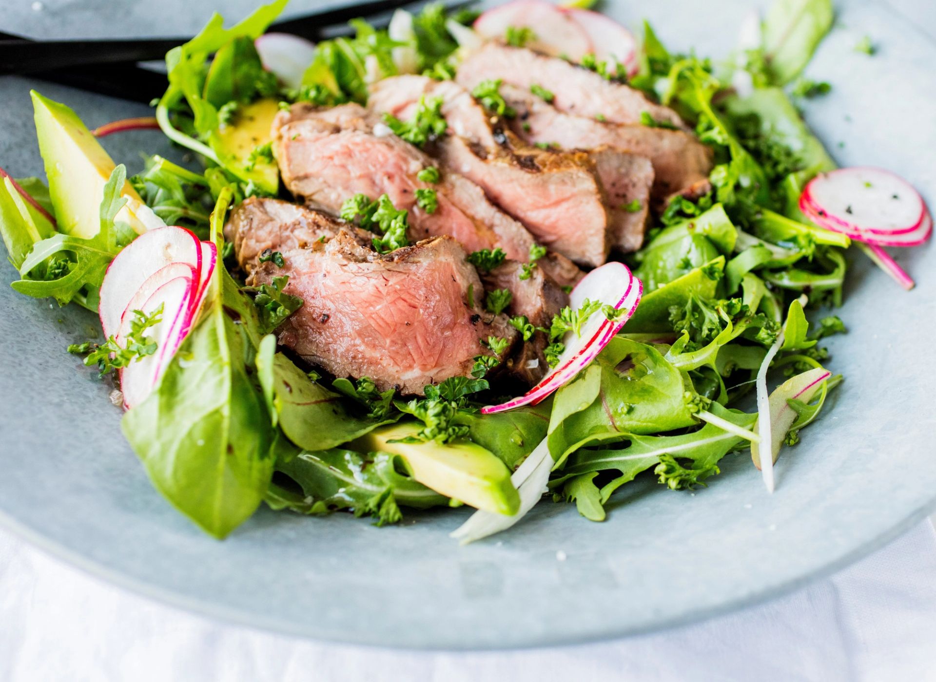 Skivet, stekt kjøtt lagt på en seng av grønne salatblader, toppet med urter, tynne skiver av reddik og avokado. 