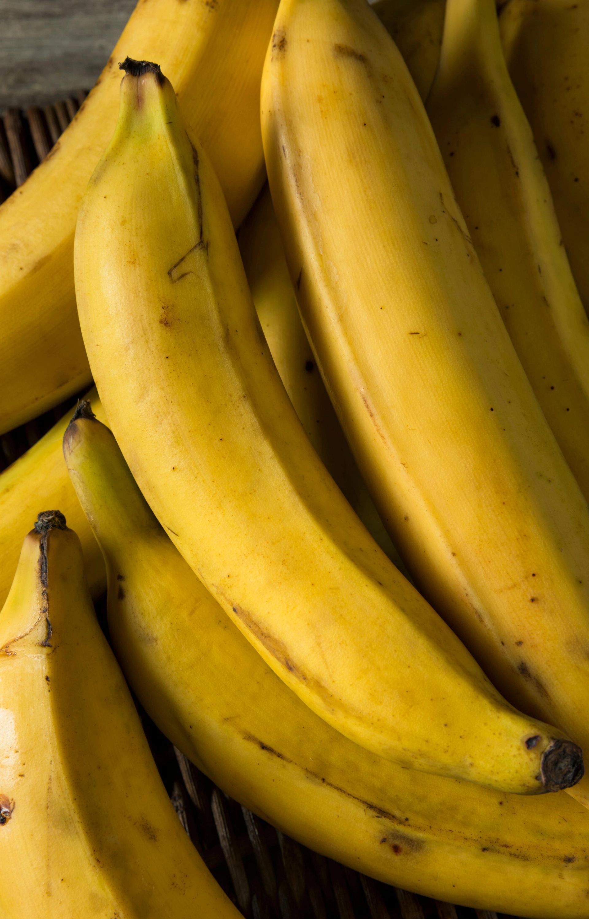 Kokebananer (plantain) samlet tett i en kurv, med lange, kraftige, gule frukter som har tykkere skall og mørke flekker. Bananene ligger tett mot hverandre og fyller hele bildeflaten.