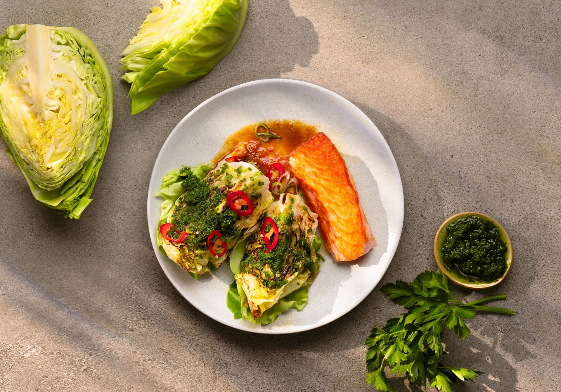 Ovnsbakt sommerkål servert med laks, chimichurri og vårløk på en tallerken.