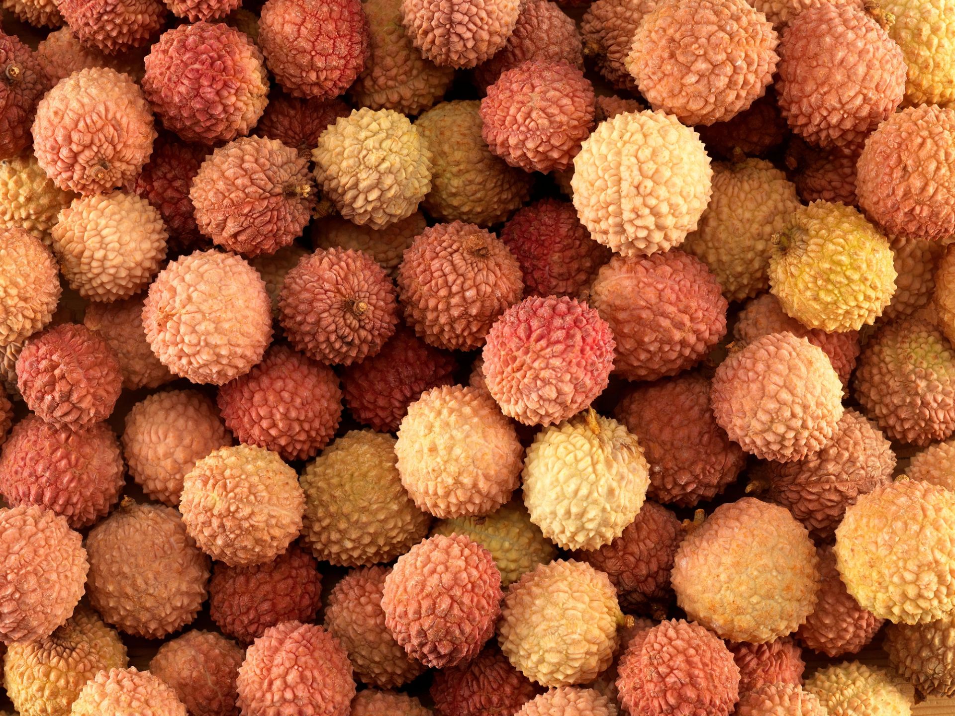 En stor haug med lychee-frukter med rødt og rosa knudrete skall, tett pakket sammen