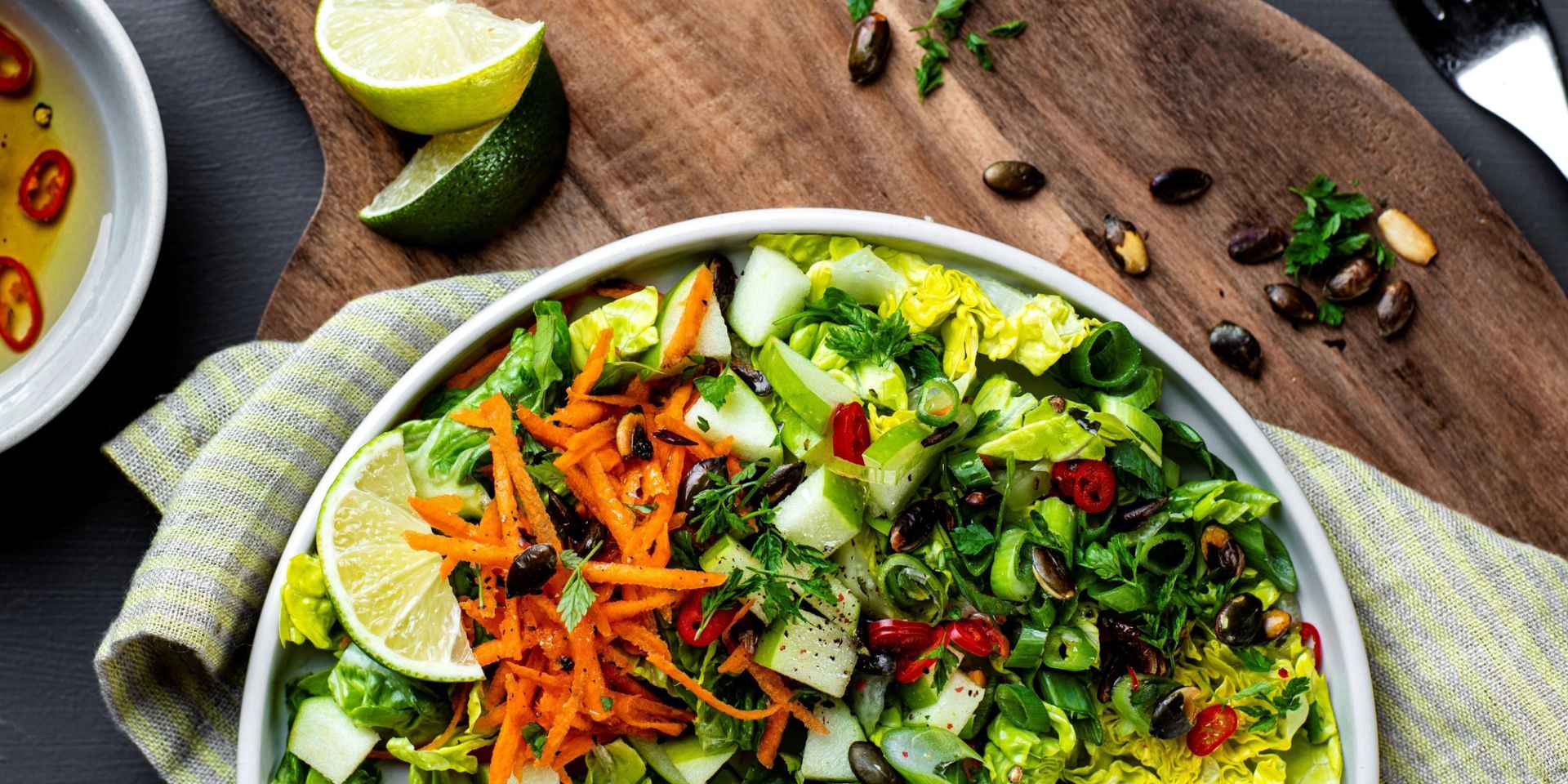 Sprø grønn sidesalat med salatblader, revet gulrot, chili, gresskarkjerner og frisk chili- og ingefærdressing, servert med lime.