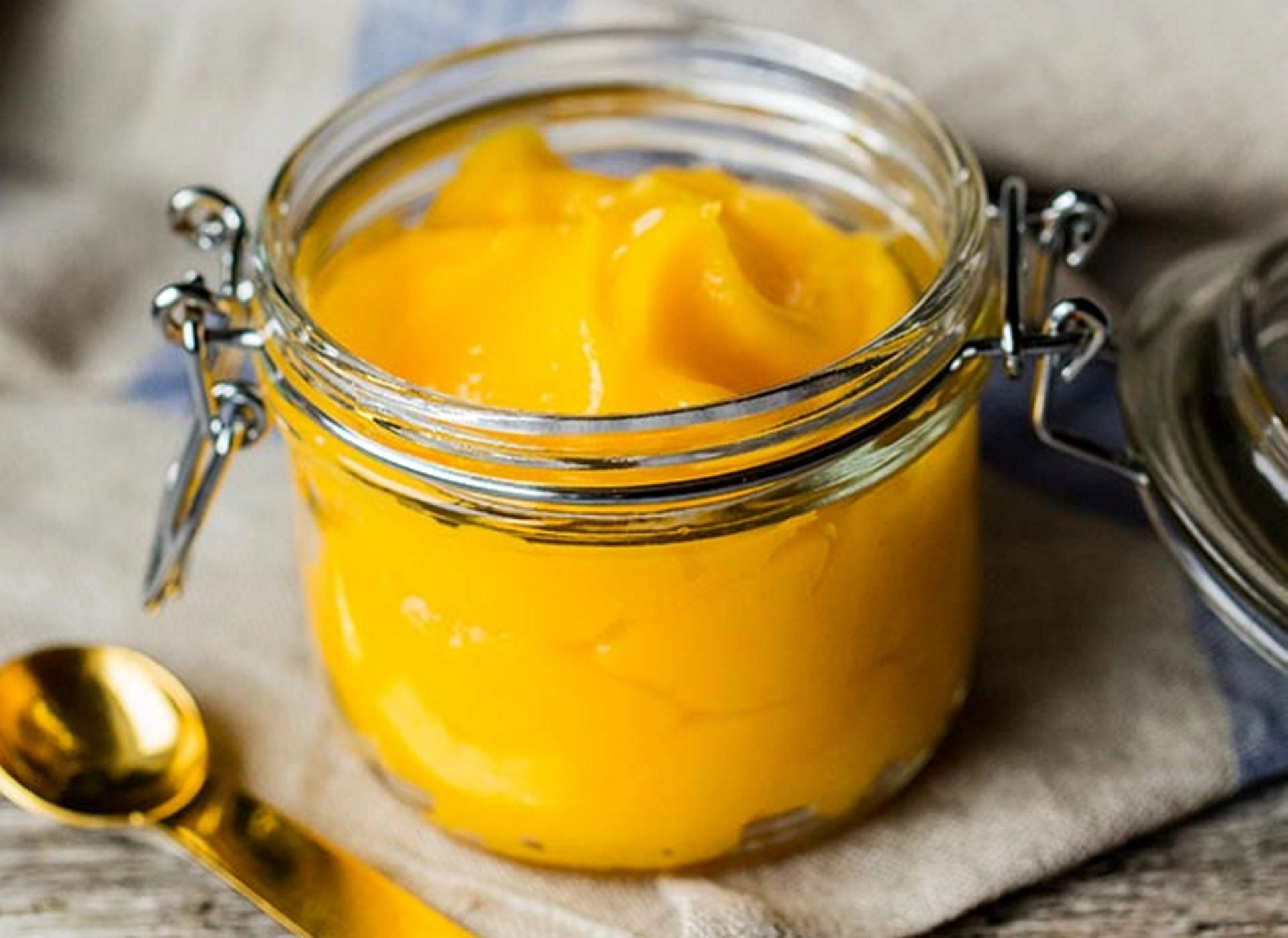 Hjemmelaget lemon curd (sitronkrem) i glasskrukke med lokk, plassert på et kjøkkenhåndkle.