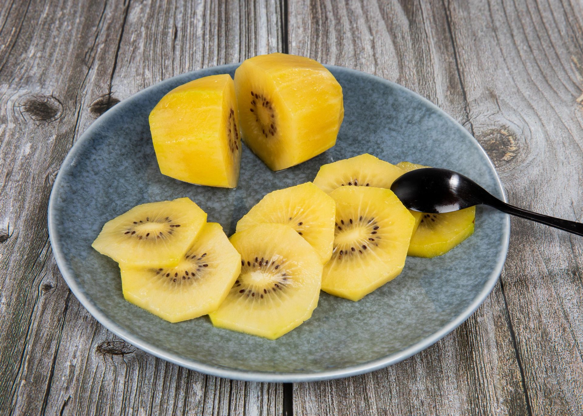 Skiver av gul kiwi arrangert på en blågrå tallerken, med to større biter øverst, plassert på et rustikt trebord.