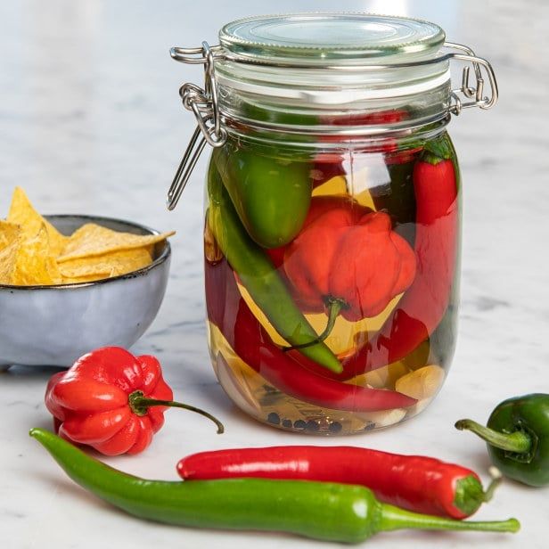 Glass med syltede chili i ulike farger, omgitt av friske chili og en liten skål tortillachips.