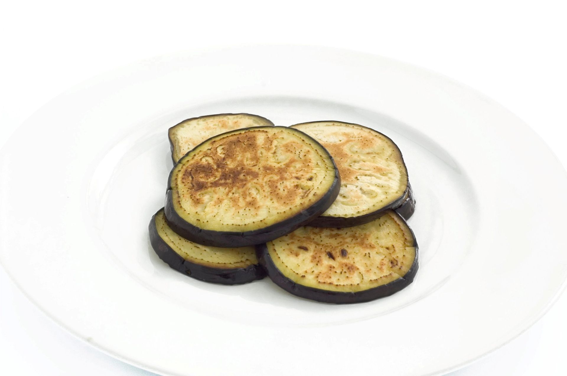 Skiver av stekt aubergine med gyldenbrun overflate og mørkt skall, servert på en hvit tallerken mot en lys bakgrunn.