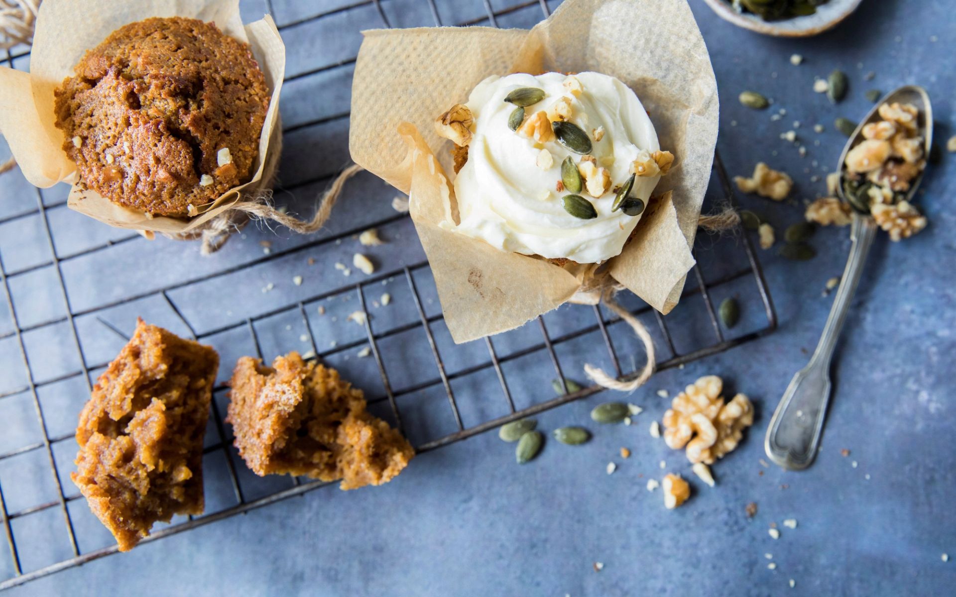 Gresskarmuffins avkjølt på rist, toppet med kremostglasur, gresskarkjerner og valnøtter.