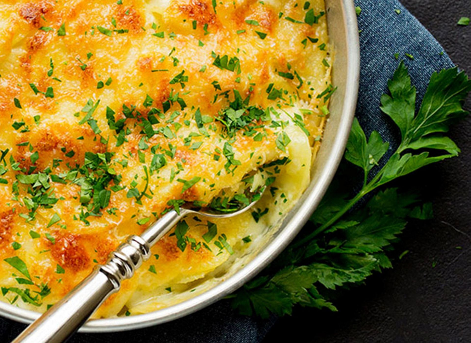Fløtegratinerte poteter med gyllen, gratinert osteskorpe og frisk persille i en ildfast form.