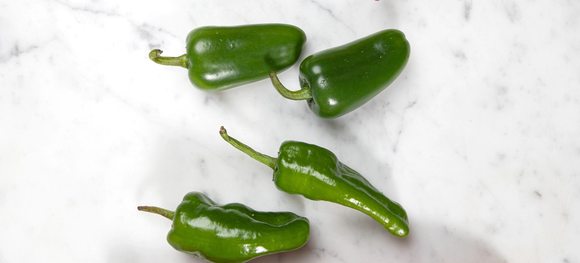 Ulike typer chilipepper i rødt og grønt arrangert på lys marmorbakgrunn.
