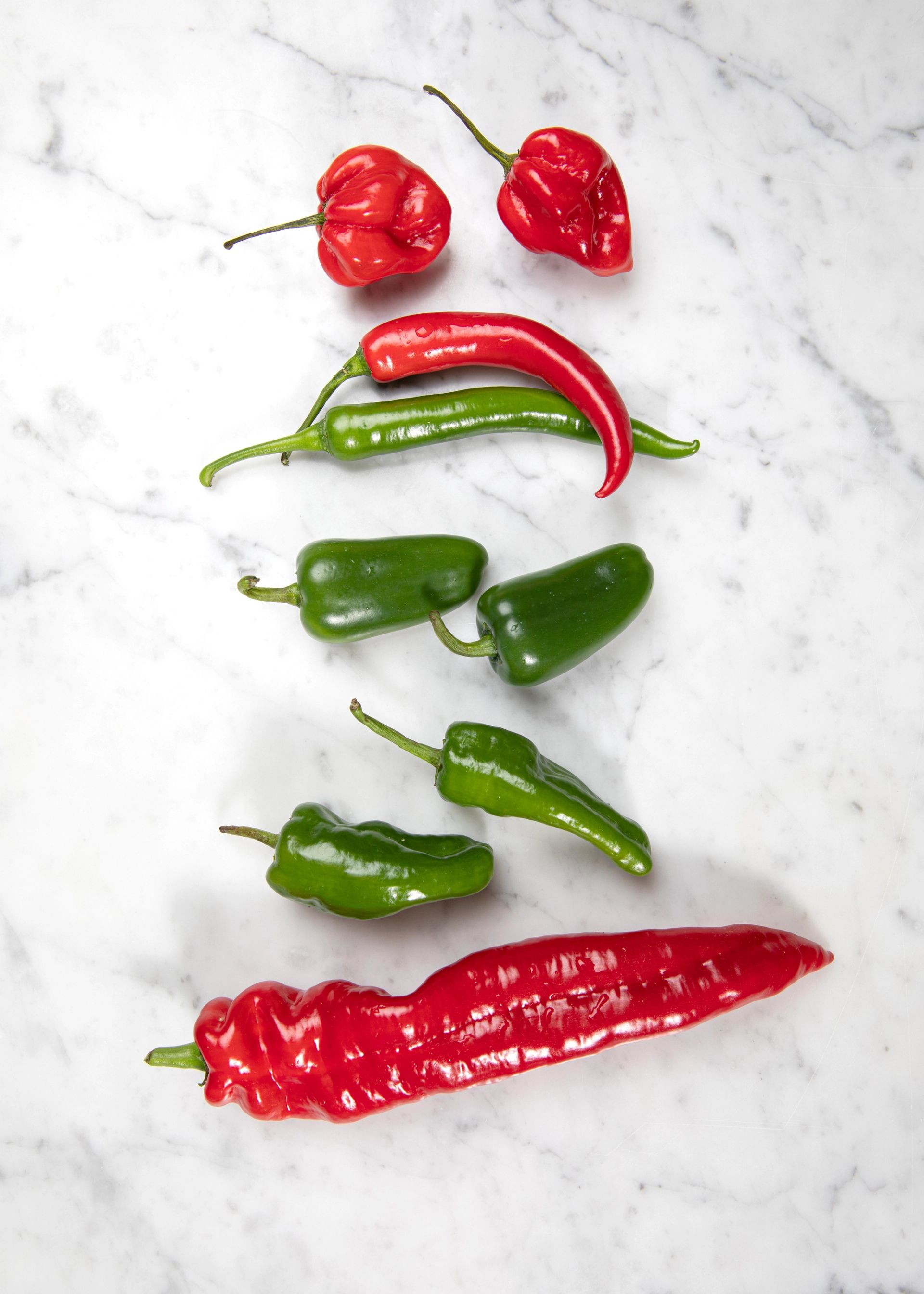 Ulike typer chilipepper i rødt og grønt arrangert på lys marmorbakgrunn.