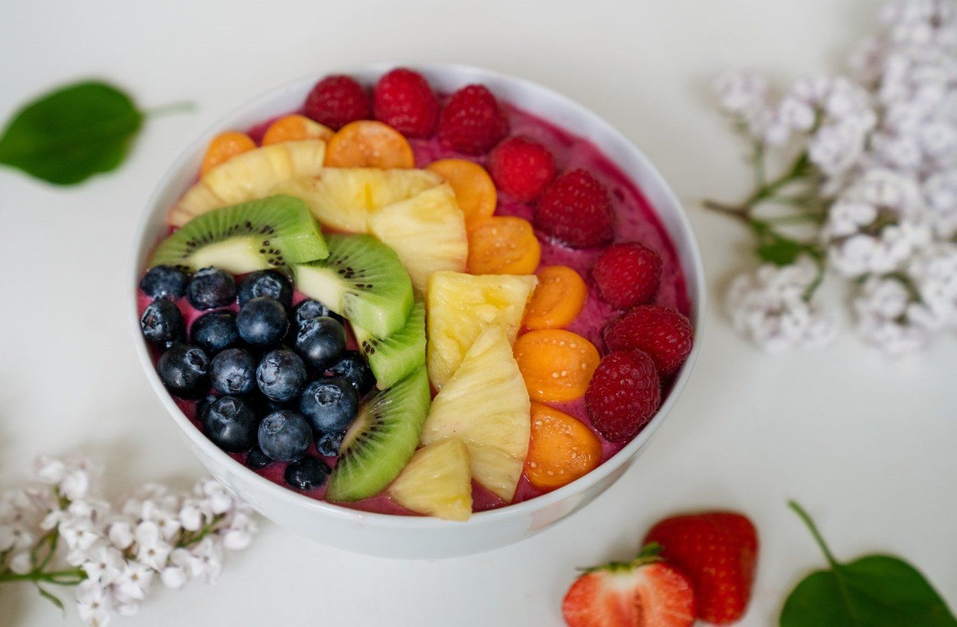 Regnbue‑smoothie bowl toppet med blåbær, kiwi, ananas, melon og bringebær i fargerikt mønster.