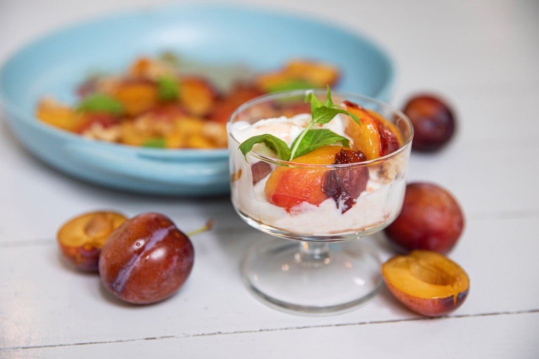 Bakte plommer med vanilje servert i dessertglass med krem, toppet med nøtter og sitronmelisse.