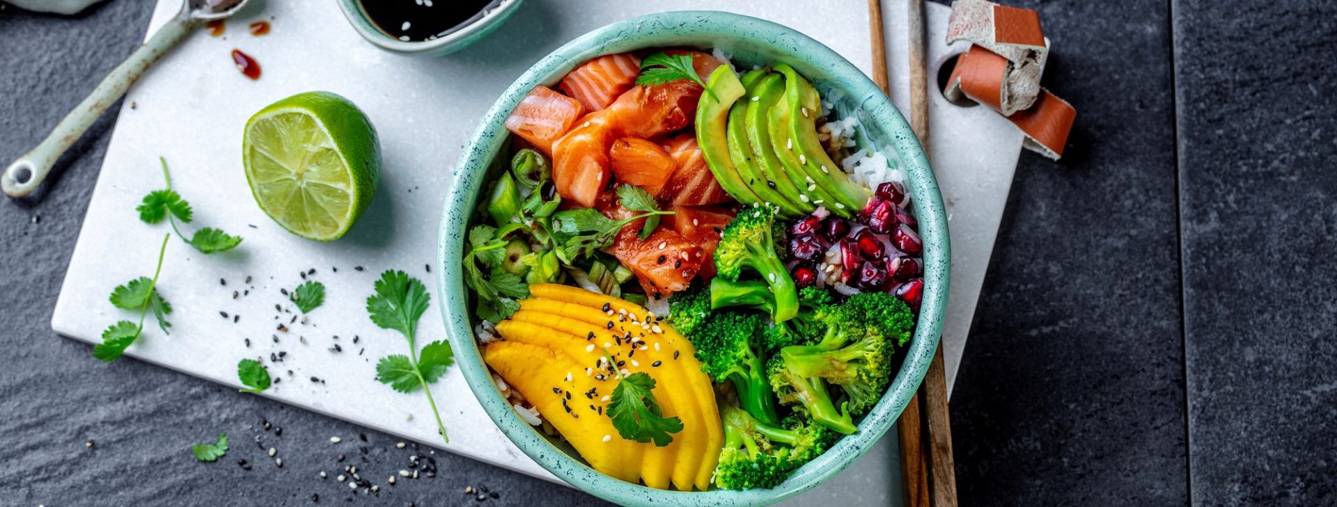 Poke bowl med fersk laks, brokkoli, avokado, mango, granateple og ris toppet med sesamfrø og koriander