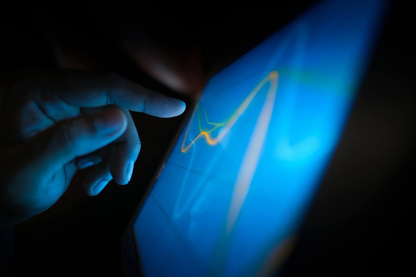 A person using a touchscreen tablet showing a line graph in the dark.