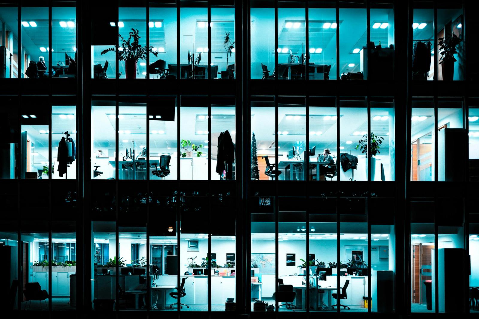 A corporate office building at night, from the outside looking in.