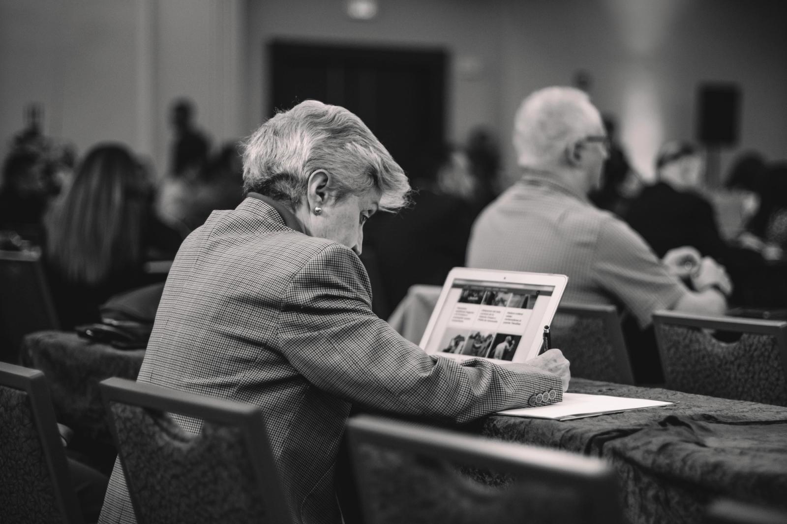 A woman sitting in a conference room taking notes while using her laptop.