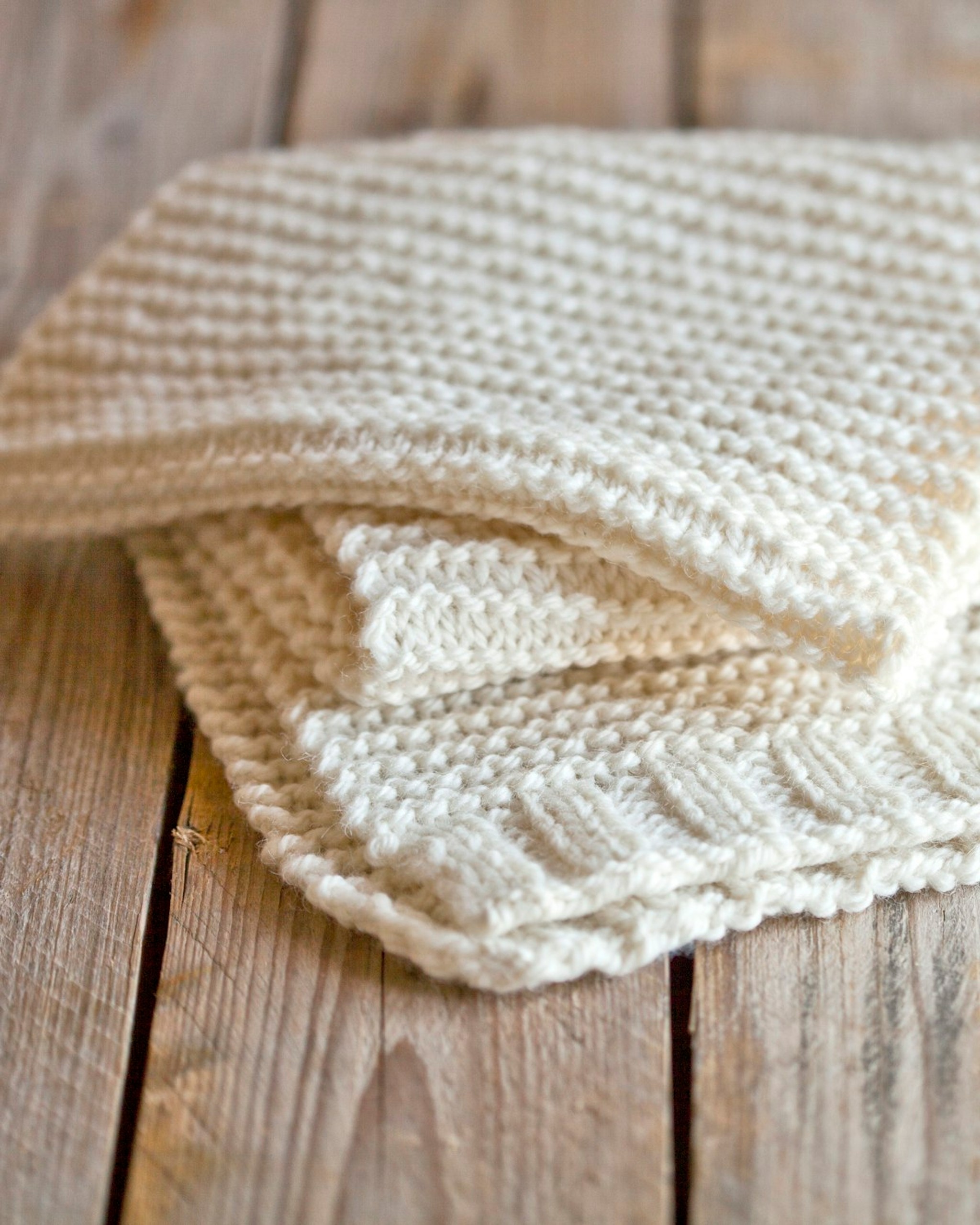 Folded cream knitted baby blanket on a wooden floor