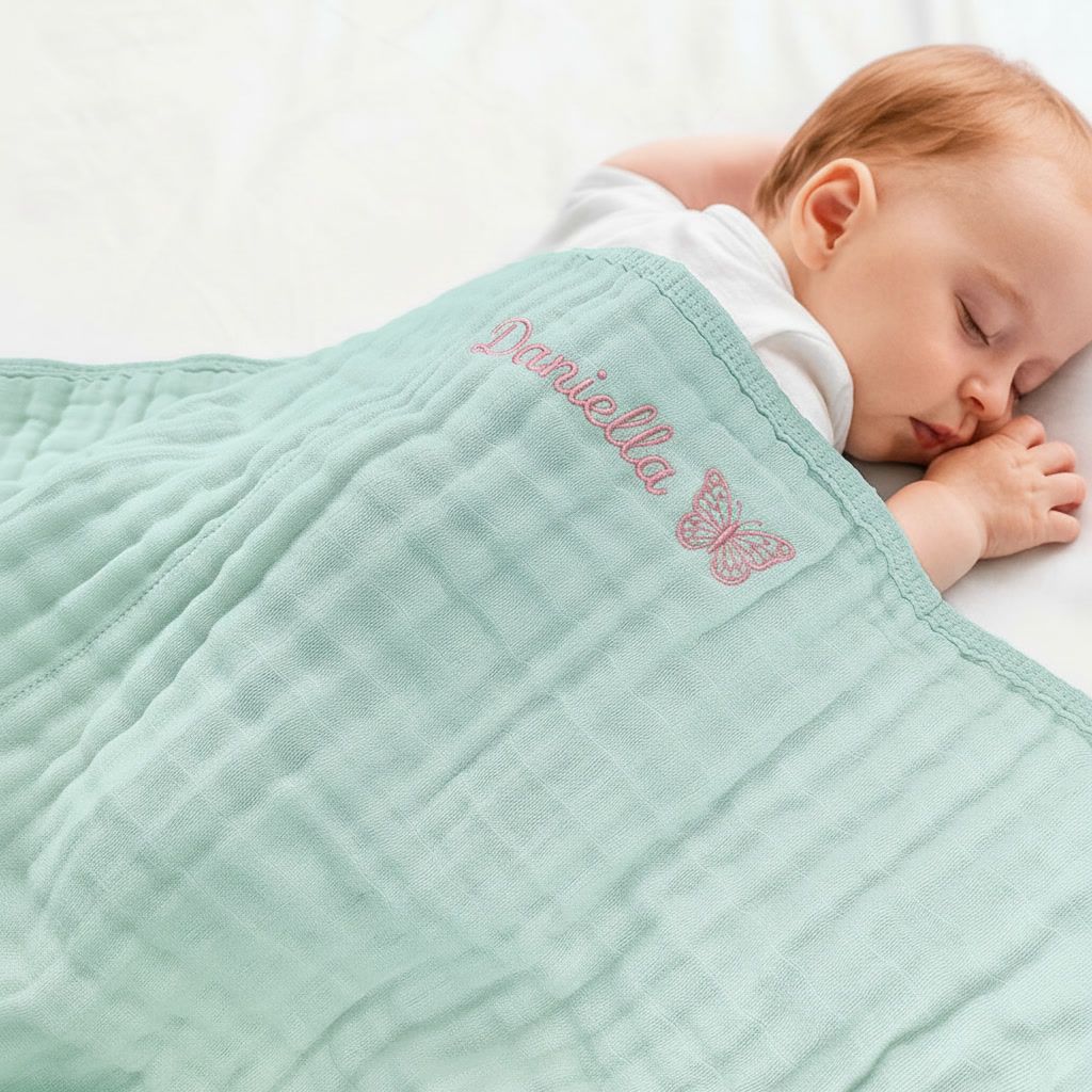 Newborn baby covered in blue muslin swaddle embroidered with baby name