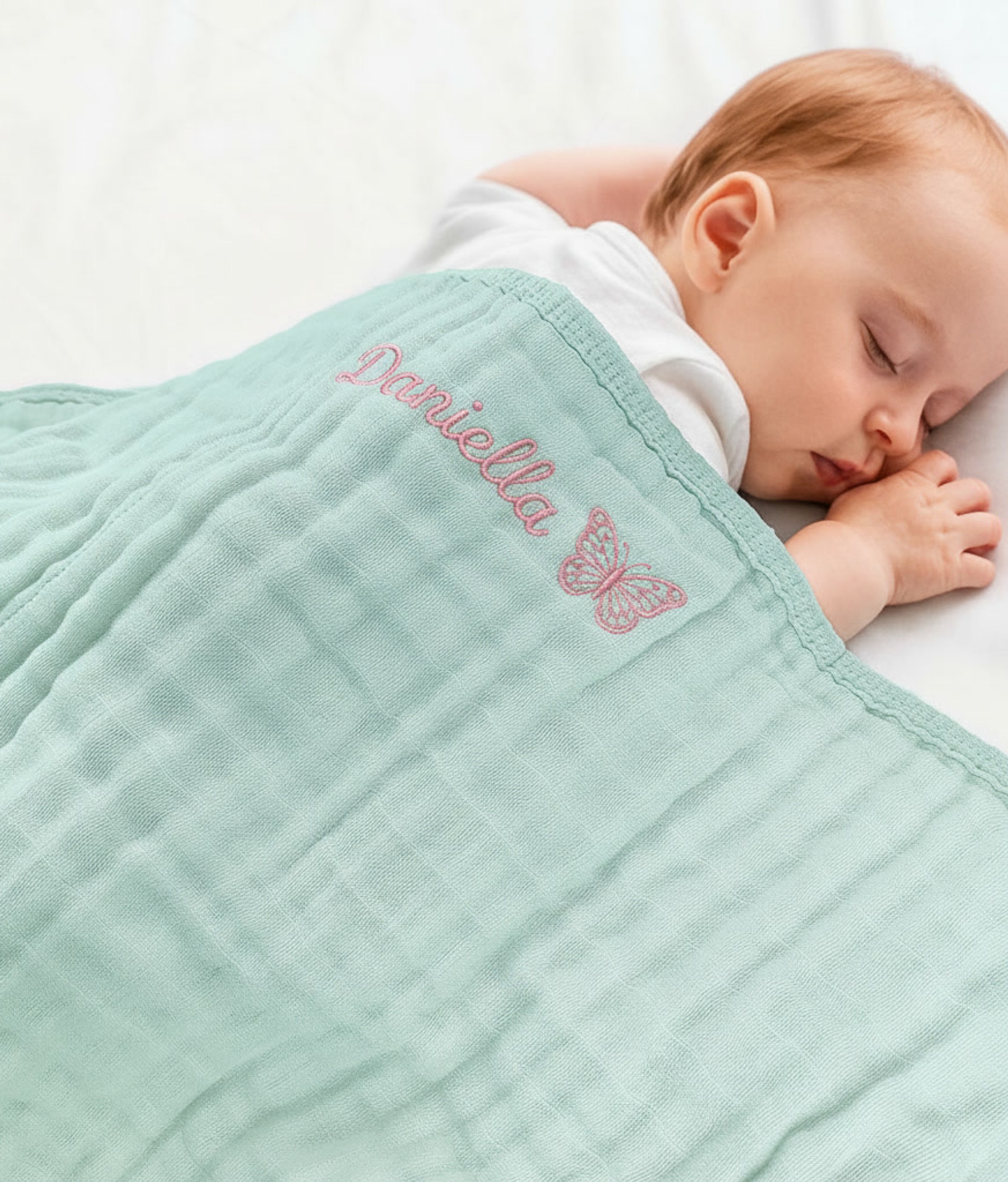 Newborn baby covered in blue muslin swaddle embroidered with baby name