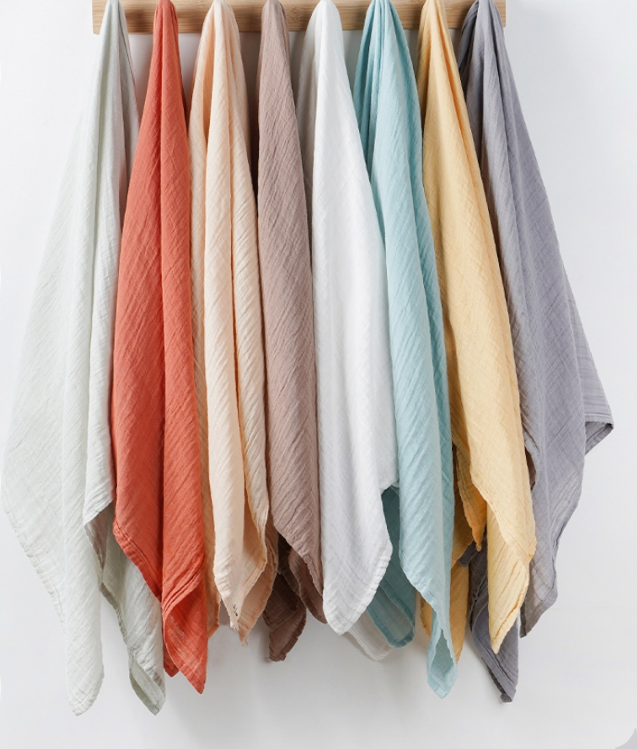 Stack of hung swaddles in grey, bric, beige,white, blue,yellow and sage