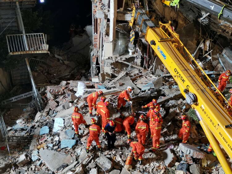 Rescue workers work next to a crane at the site where a hotel building collapsed in Suzhou