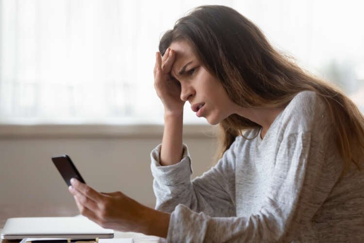 Frustrated young woman struggles with smartphone, highlighting social media scams - Global Banking & Finance Review