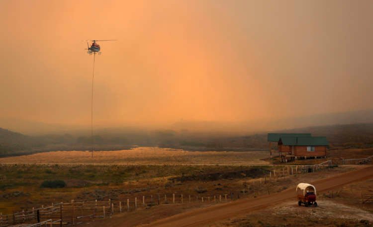 A firefighting helicopter fills a bucket of water in heavy smoke as the North Merna wildfire burns in the Bridger National Forest west of the town of Pinedale in Sublette County, Wyoming