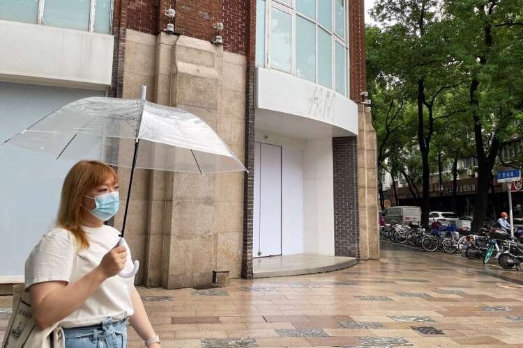 Woman walks by a boarded-up H&M flagship store in Shanghai, highlighting consumer backlash - Global Banking & Finance Review