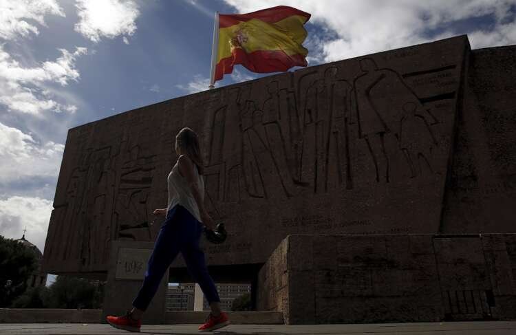 A woman walks past the Discovery Monument in Madrid with a large Spanish flag, representing Spain's new work visa policy - Global Banking & Finance Review