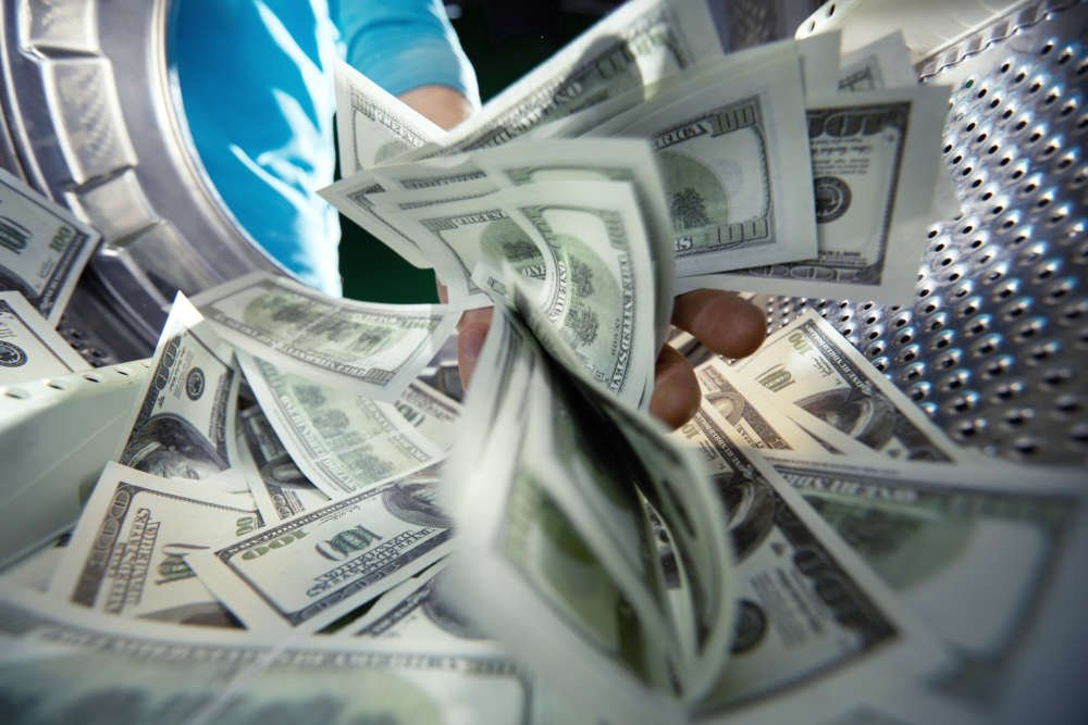 Criminal washing banknotes in a machine, illustrating money laundering risks in business - Global Banking & Finance Review