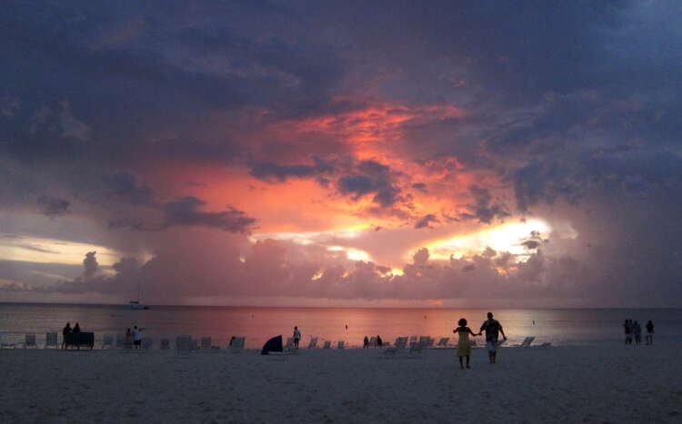 FILE PHOTO: Tourists walk on Seven Mile Beach at sunset in George Town, Cayman Islands