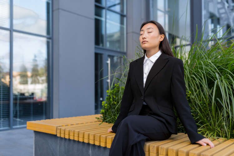Beautiful Asian business woman meditating outdoors, embodying mindfulness in business - Global Banking & Finance Review