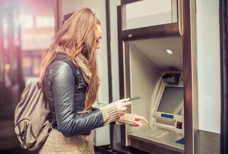 Young woman withdrawing cash from ATM, symbolizing banking's role for youth - Global Banking & Finance Review