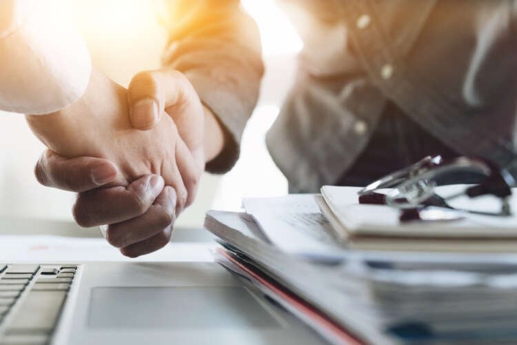 Business professionals shaking hands to signify a bank merger - Global Banking & Finance Review