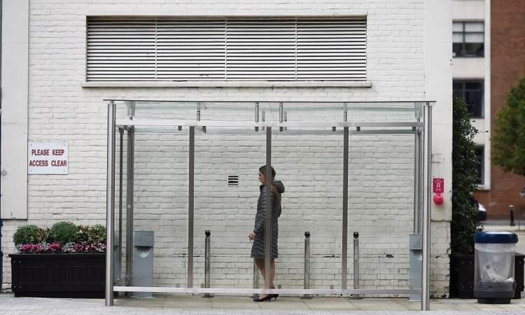 A woman smoking in a glass shelter in London, highlighting tobacco use amidst proposed age restrictions - Global Banking & Finance Review