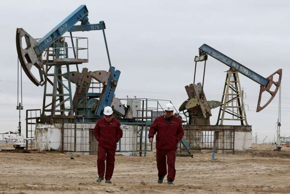 FILE PHOTO: Workers walk as oil pumps are seen in the background in the Uzen oil and gas field in the Mangistau Region