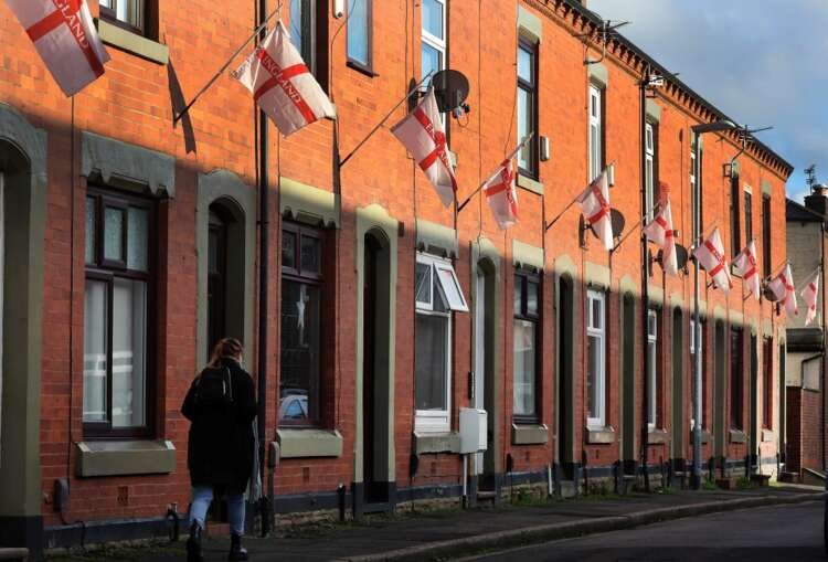 A woman walks past English flags outside houses, reflecting UK mortgage trends - Global Banking & Finance Review