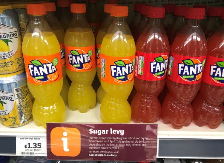 Sign indicating the UK sugar tax on soft drinks in a supermarket - Global Banking & Finance Review