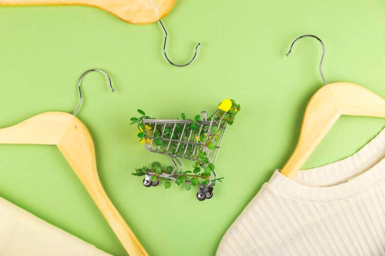 Shopping cart entwined with plants on green background among hangers. Sustainable eco lifestyle.