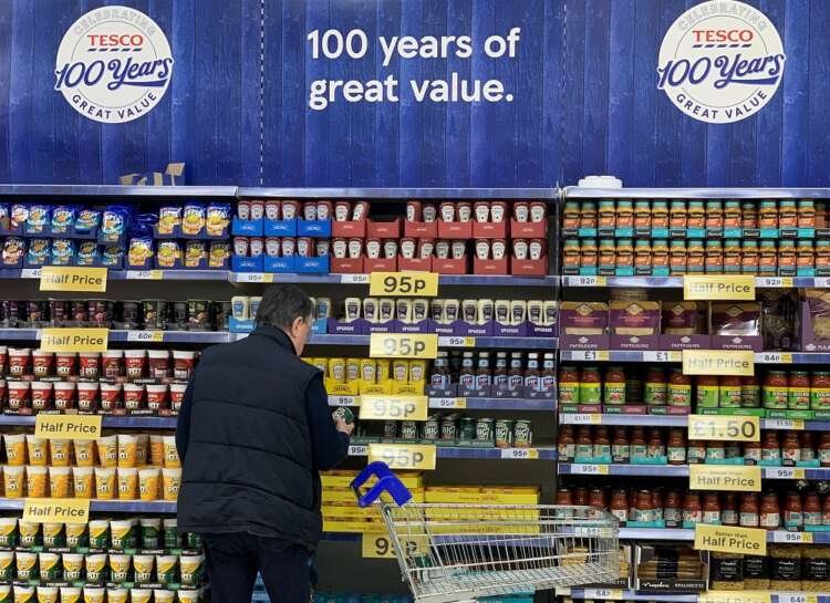 A shopper examines products on a shelf in a Tesco store, reflecting UK consumer mood amid economic challenges - Global Banking & Finance Review