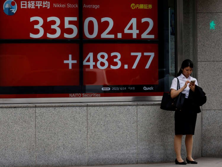 A woman checks her phone in front of a Nikkei stock display in Tokyo - Global Banking & Finance Review