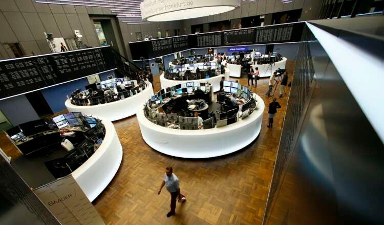 Traders work at their desks in front of the German share price index, DAX board, at the stock exchange in Frankfurt