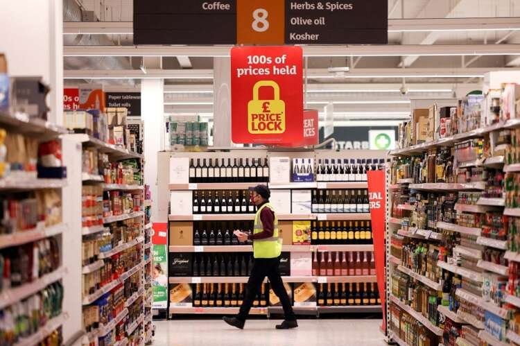 Employee stocking shelves in Sainsbury's, highlighting price stability amid inflation - Global Banking & Finance Review