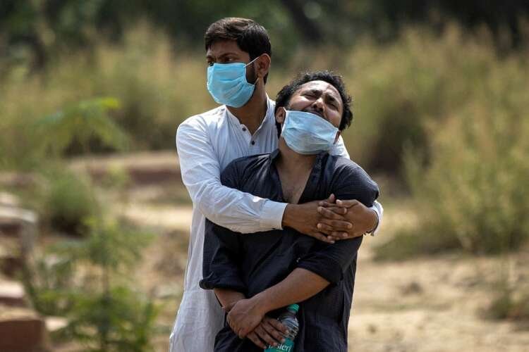 A grieving man is consoled before his father's burial in New Delhi, highlighting COVID-19's tragic toll - Global Banking & Finance Review