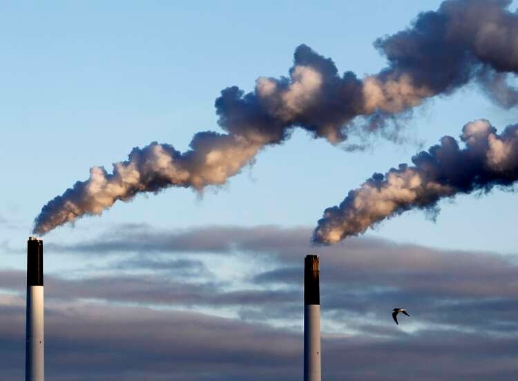 Bird flying near chimneys emitting smoke in Copenhagen's harbour area - Corporate carbon tax news - Global Banking & Finance Review