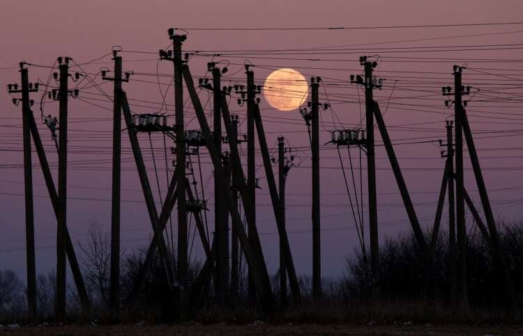 Electric poles silhouetted against a rising full moon, symbolizing energy transition - Global Banking & Finance Review